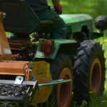 Rear view of a man using a tractor mower in a lush green field during summer.