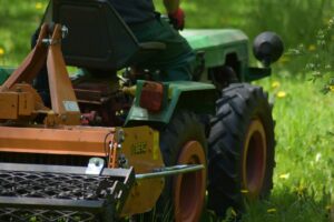 Rear view of a man using a tractor mower in a lush green field during summer.